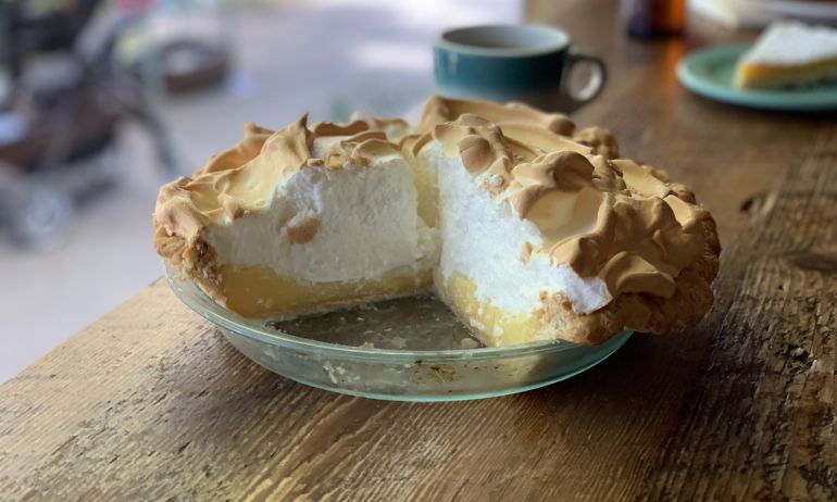 a tall lemon meringue pie with a couple of slices missing sitting in a glass pie dish