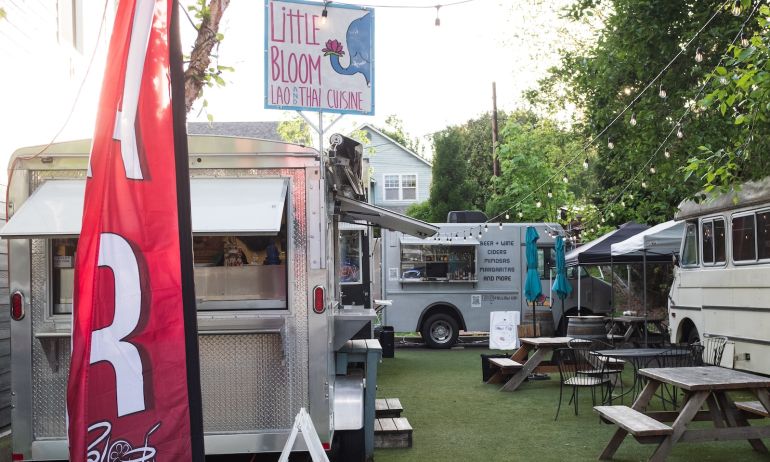 A food cart pod with food trucks gathered around a small seating area with picnic tables.