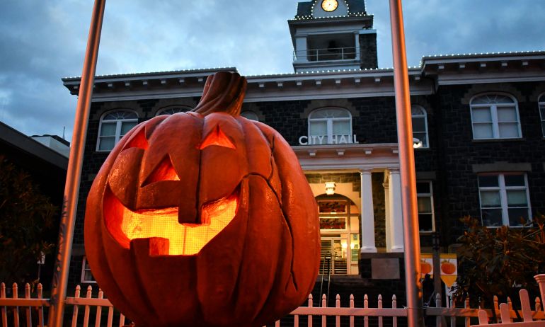 a giant pumpkin sculpture is lit on the inside sitting in front of a town hall building