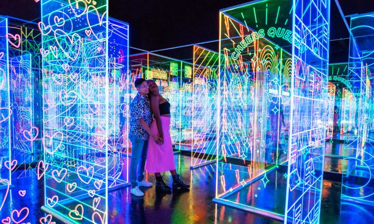 People move through a darkened space between large, clear panels illuminated with attractive glowing patterns.