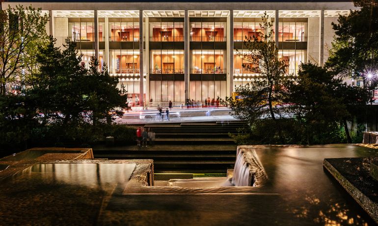 exterior of the Keller Auditorium at night showing a wide building lit from within, viewed from the Keller Fountain, whose geometric lines mirror the auditorium\'s architecture