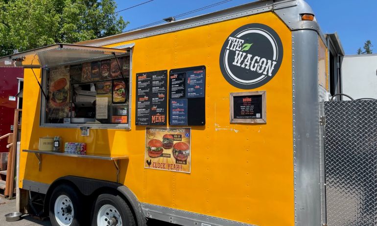 a bright yellow food cart advertising plant-based food with a circular sign reading “The Wagon”