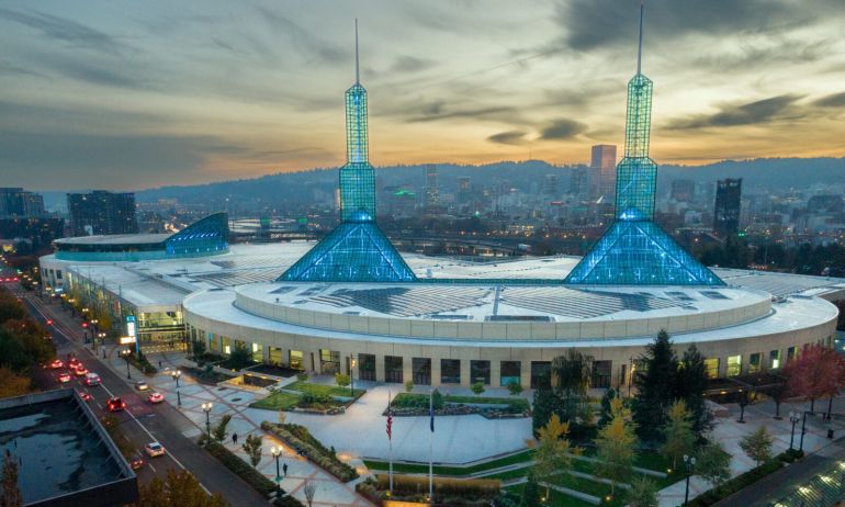 a vast building with two spires at sunset with the city skyline and hills in the background