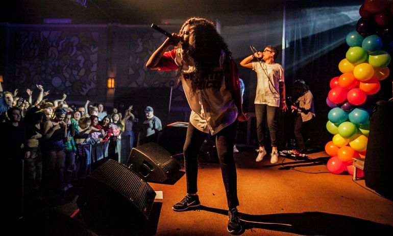 two hip hop performers sing into microphones on stage in front of an excited audience