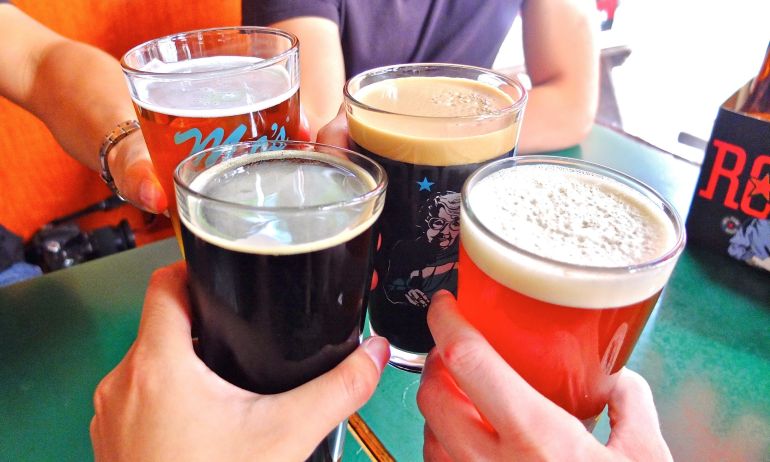 four hands raise four pints of Rogue beer in a toast