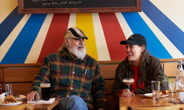 Two people sit and laugh with food and drink in a restaurant