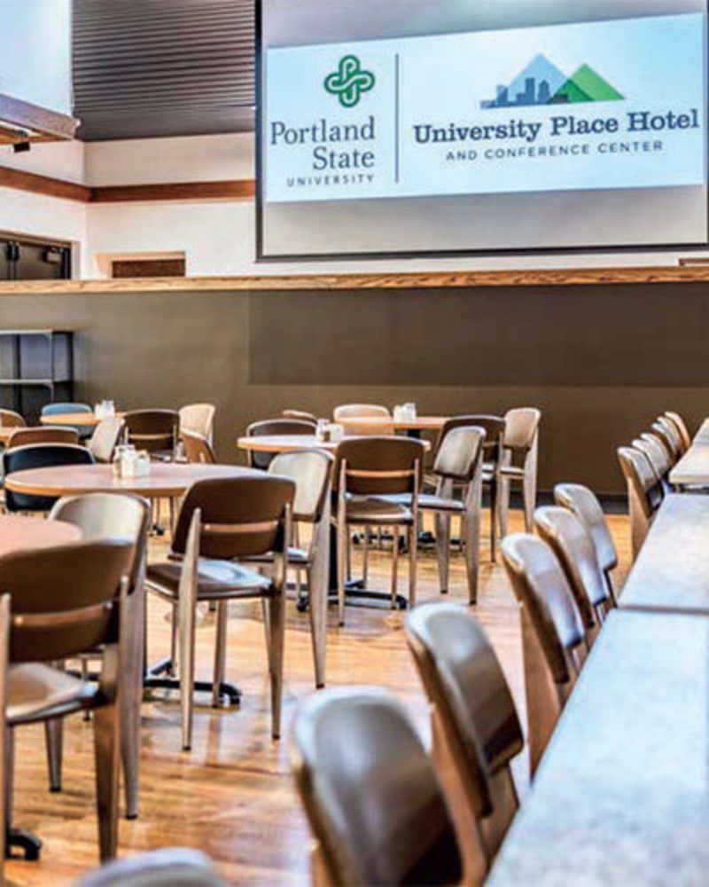 conference room set up with tables and chairs and a large screen at the University Place Hotel
