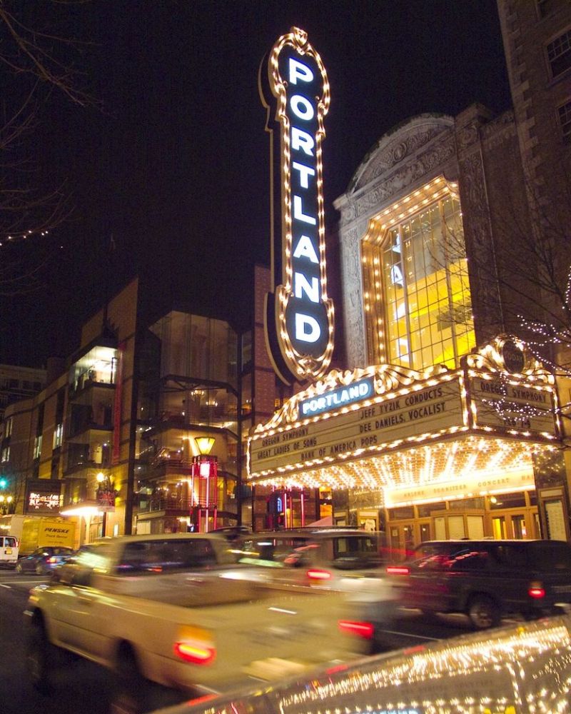 The iconic Portland sign lights up the night as cars stream past the Arlene Schnitzer Concert Hall.