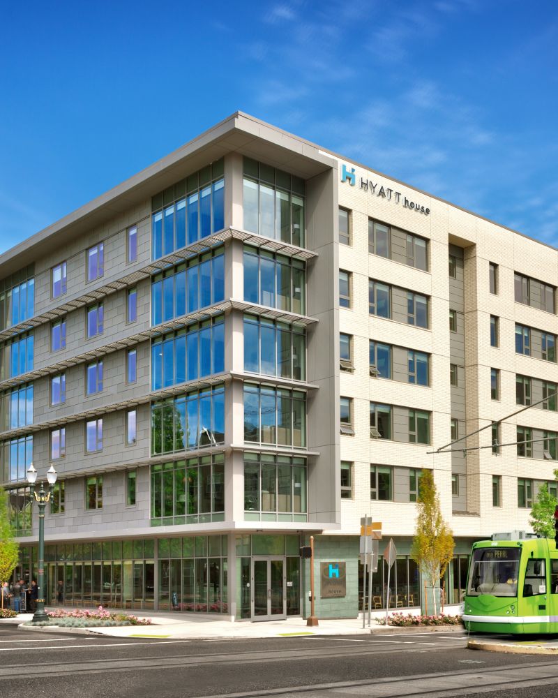 Exterior view of Hyatt House Hotel with six stories and a green max train running in front