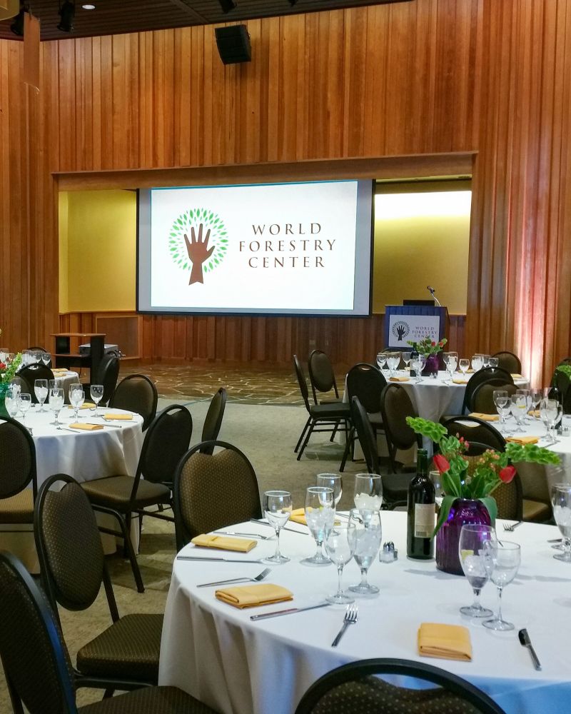 social event setting with large round tables directed toward a large screen and podium