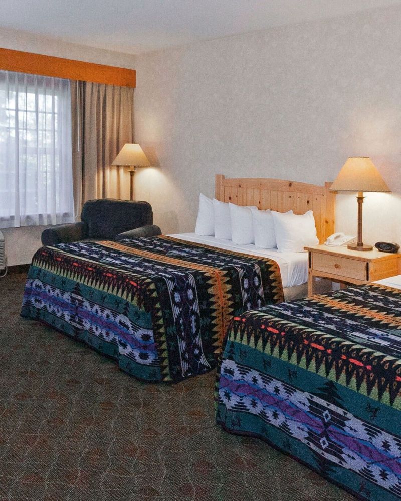 two queen sized beds covered with colorful blankets with geometric patterns in a hotel room