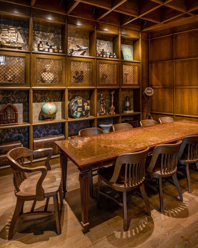 a sturdy wooden table surrounded by chairs with a shelf of curios in the background