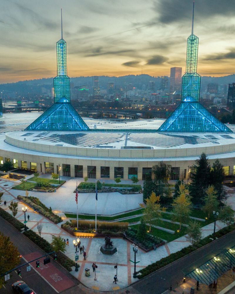 a vast building with two spires at sunset with the city skyline and hills in the background