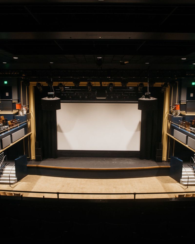 an empty auditorium with two-level seating, large speakers, a stage and a projection screen