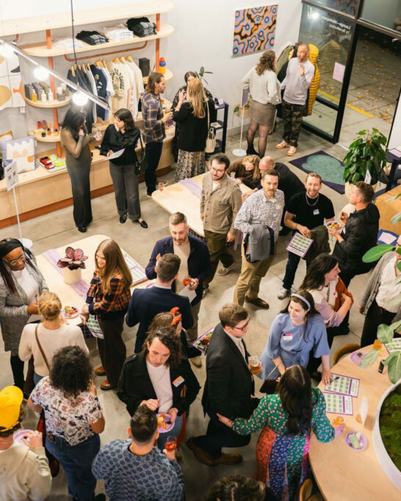 A view looking down into a large room full of people. The room is open and clean, with some clothing wares displayed on the wall and a large tree in the center of the room.