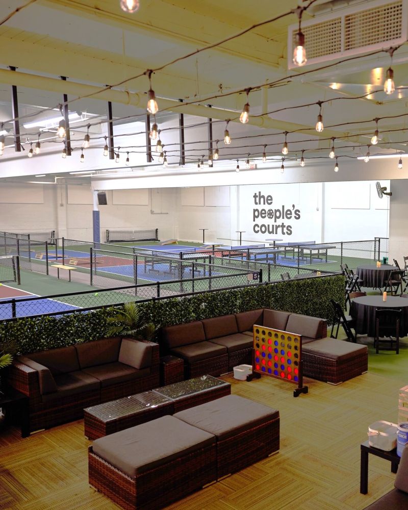 A series of tables and couches in the foreground pair with pickleball courts in the background.