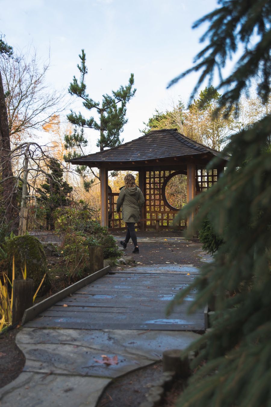 person walking in a traditional Japanese garden with a wooden bridge and structure