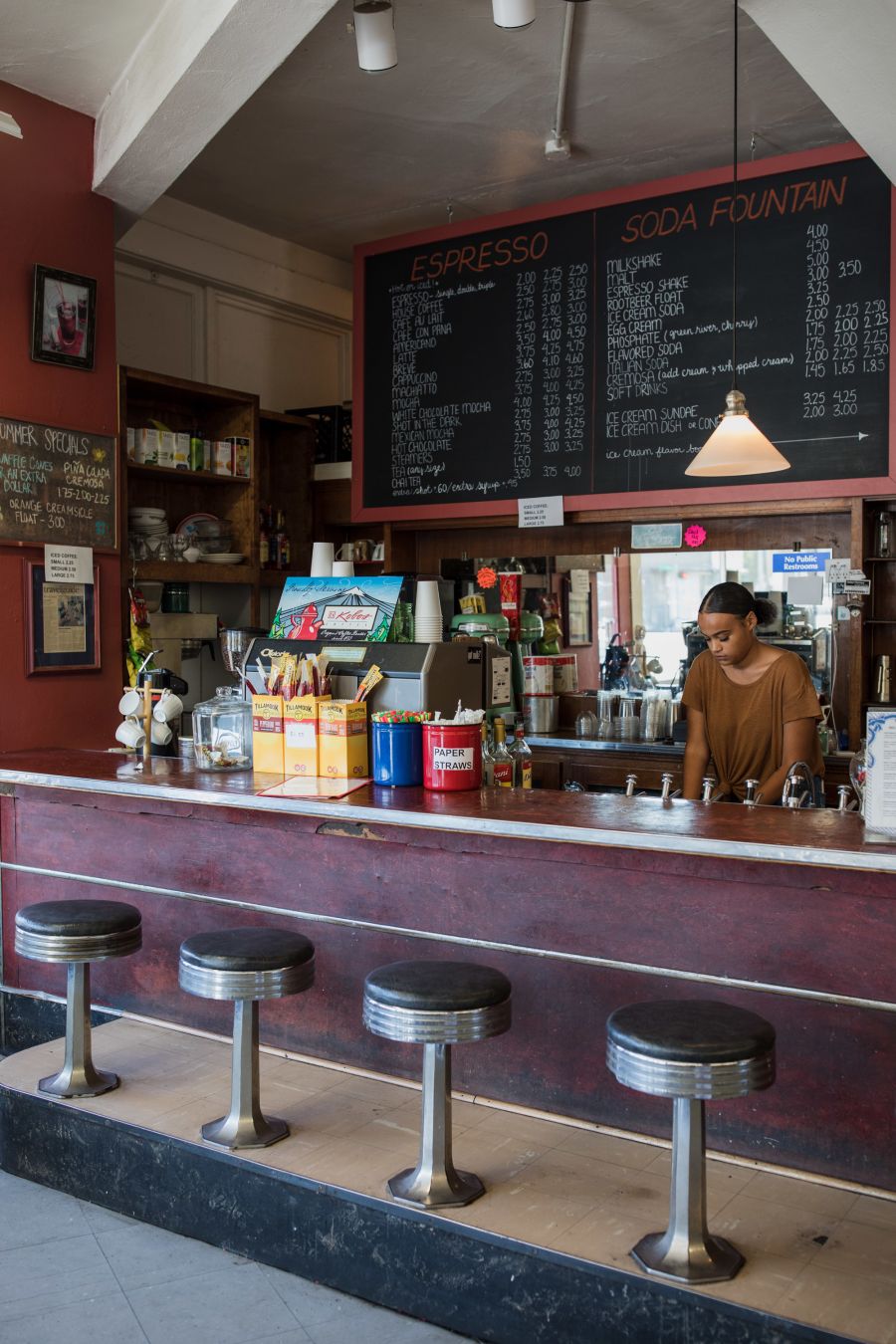 A woman works behind the counter of an old-fashioned soda fountain