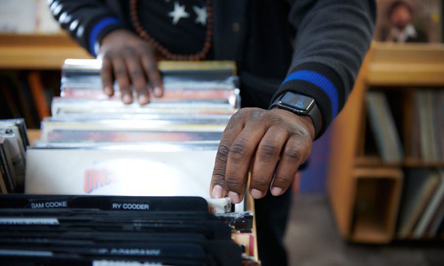 A closeup of a Black man's hands flipping through records with the labels "Sam Cooke" and "Ry Cooder" visible