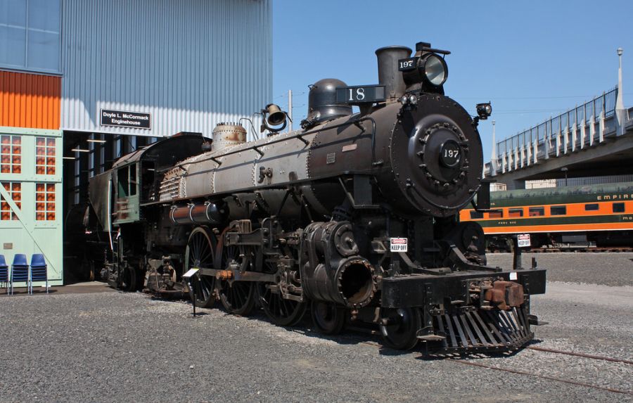 a steam locomotive on a track in front of a museum at a rail yard