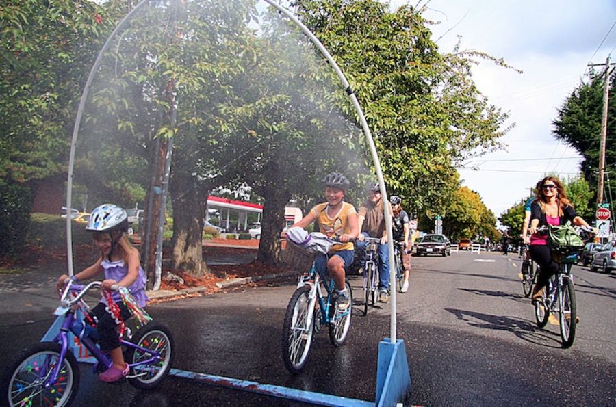 bikers riding through a water mister to cool off on a sunny day