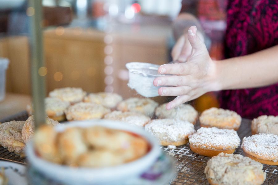 hands sprinkling powdered sugar over pastries