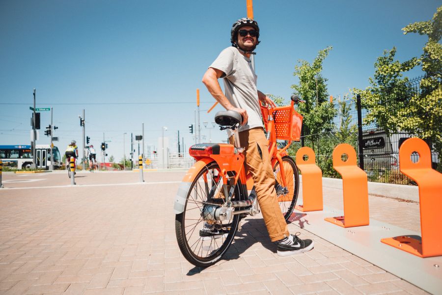 A person standing over an orange bike next to bike stands