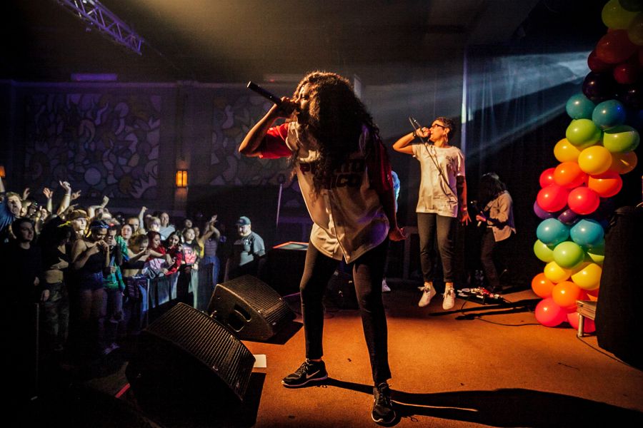 two hip hop performers sing into microphones on stage in front of an excited audience