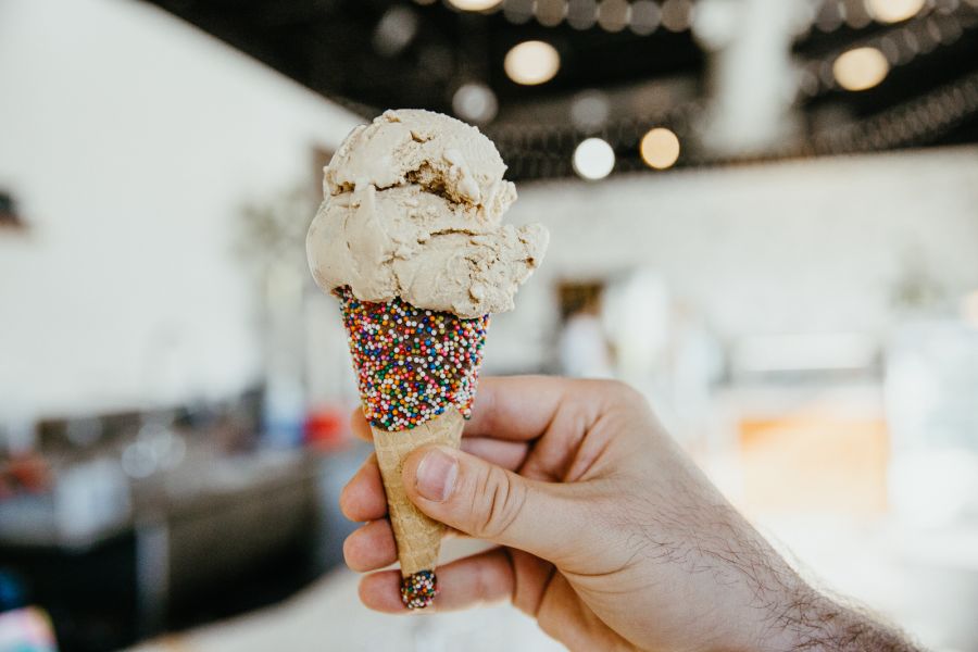 a white hand holds an ice cream cone that's coated in sprinkles