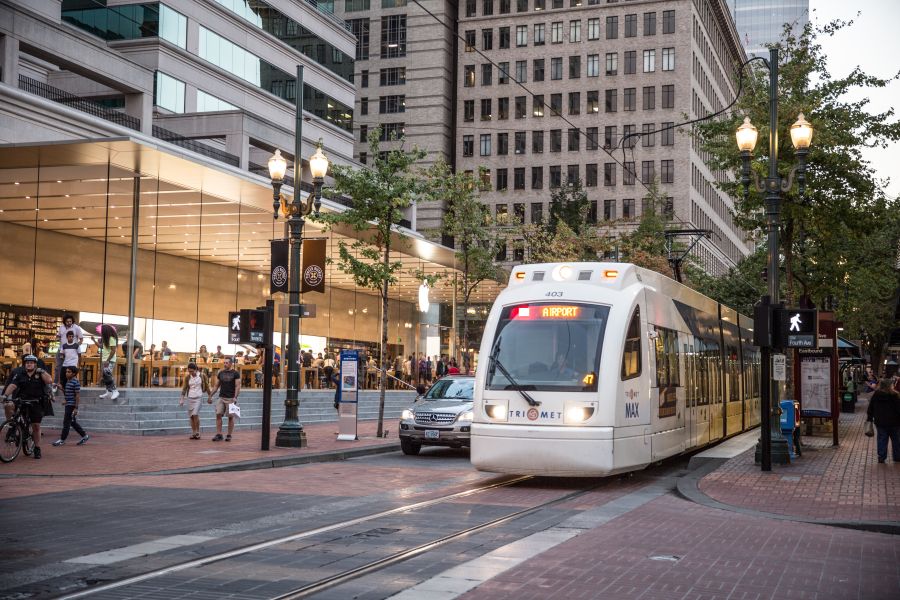 A light rail train passes in front of a modern, glass-encased retail store