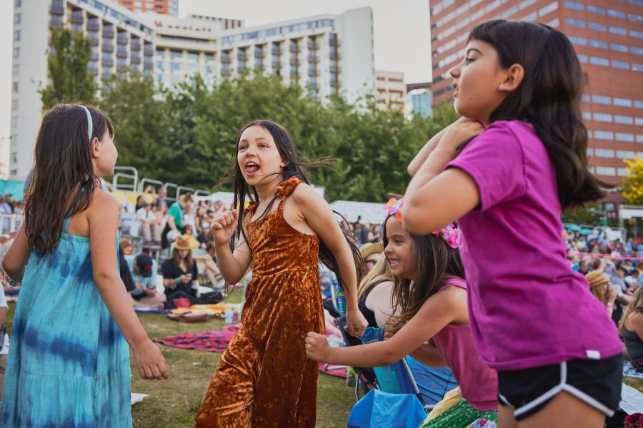 four children dancing in front of a crowd and tall buildings