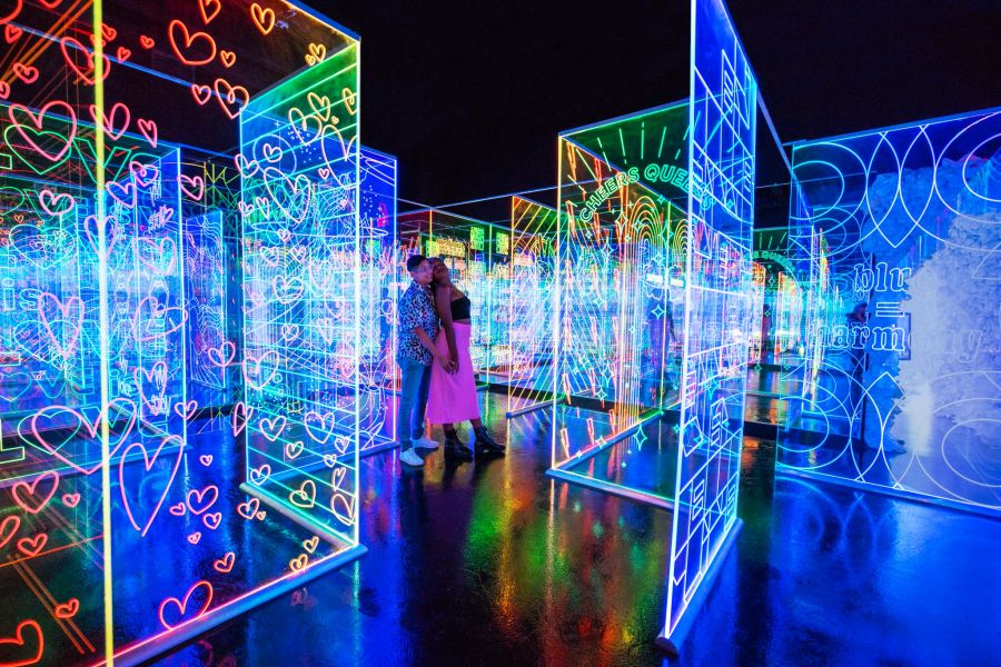 People move through a darkened space between large, clear panels illuminated with attractive glowing patterns.
