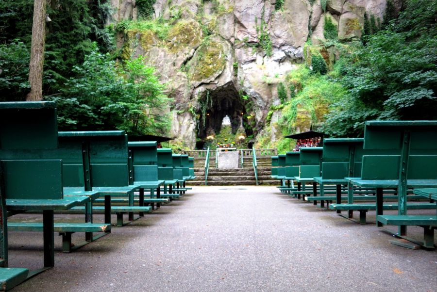 rows of benches face a rock wall and tunnel surrounded by moss, trees