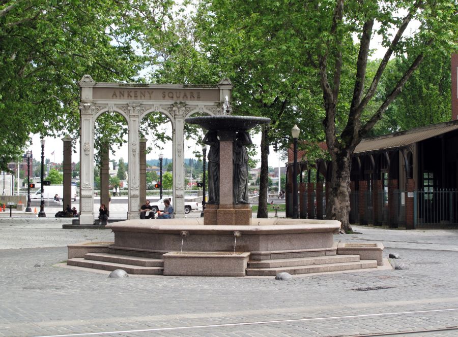 cobblestone plaza with a large, ornate fountain and a series of columns that read Ankeny Square surrounded by trees