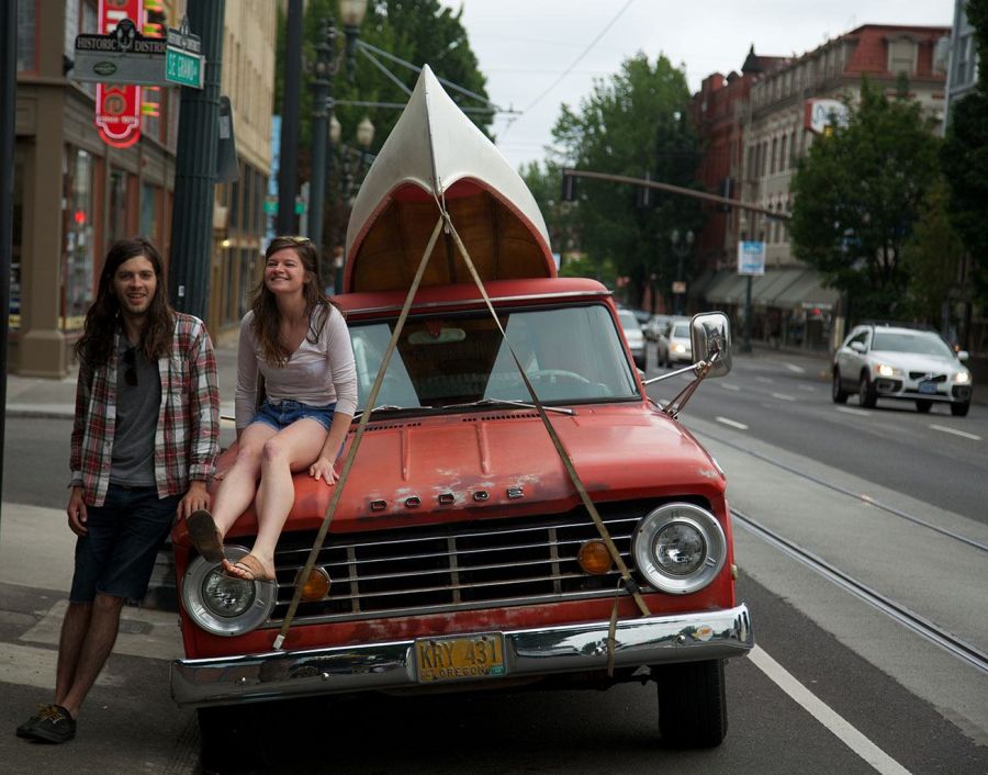 two people next to an orange truck with a canoe strapped to the top