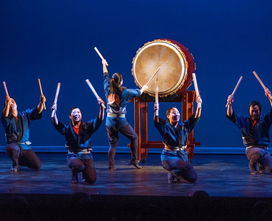 people performing on stage on large traditional japanese drums