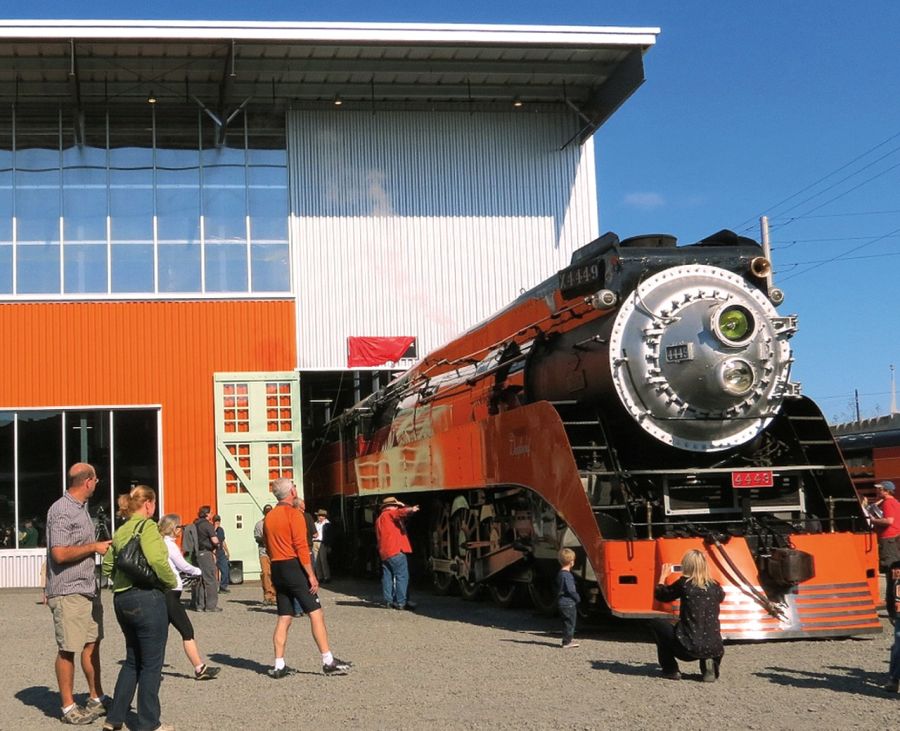 Many people are admiring a bright orange steam engine at the Oregon Rail Heritage Center.