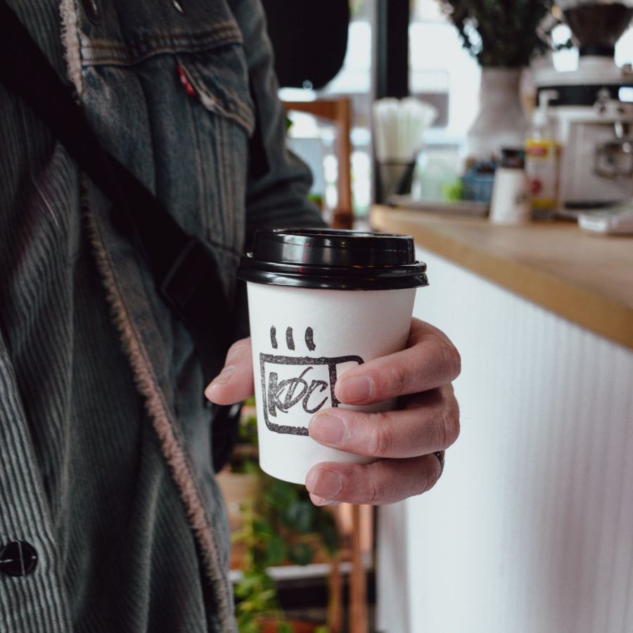 close-up of a person’s hand holding a coffee drink in a to-go cup