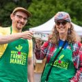 two people wearing green Rocky Butte Farmers Market aprons clink tea cups