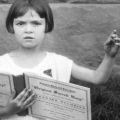 A young person looks out, holding the Sacred Harp songbook with left hand lifted to lead.