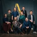 All eight members of VOCES8 causally dressed posing in a photo studio infront of a gray backdrop.