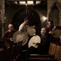 All four members of Tambuco sitting in a stone church or mission playing bodhran drums.