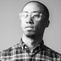 black and white head shot of a person in a plaid shirt and glasses