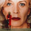 a person in a red coat stand in front of an large image of a face