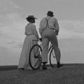 a black and white image of a woman walking next to a man and a bicycle