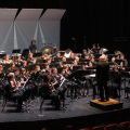 A large wind ensemble with the conductor standing in front directing.