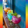 a line of colorful cocktails in stemware on a counter
