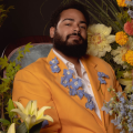 headshot of a man in a yellow suit jacket surrounded by flowers