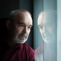 man standing next to a window showing his reflection