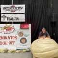 a man poses with a giant pumpkin being weighed